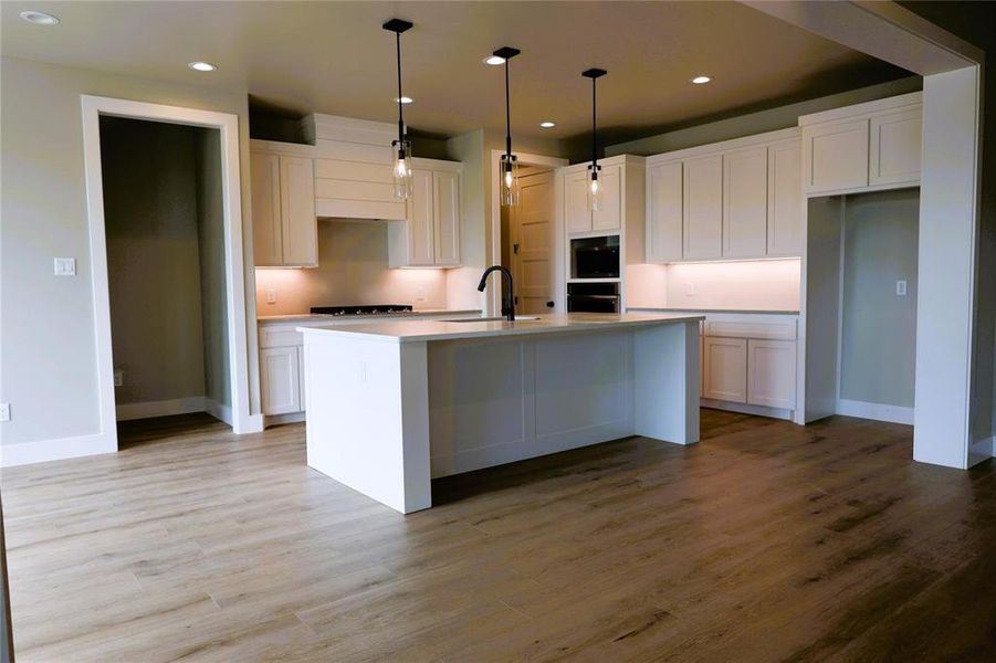 Kitchen featuring white cabinetry, an island with sink, and light wood-type flooring