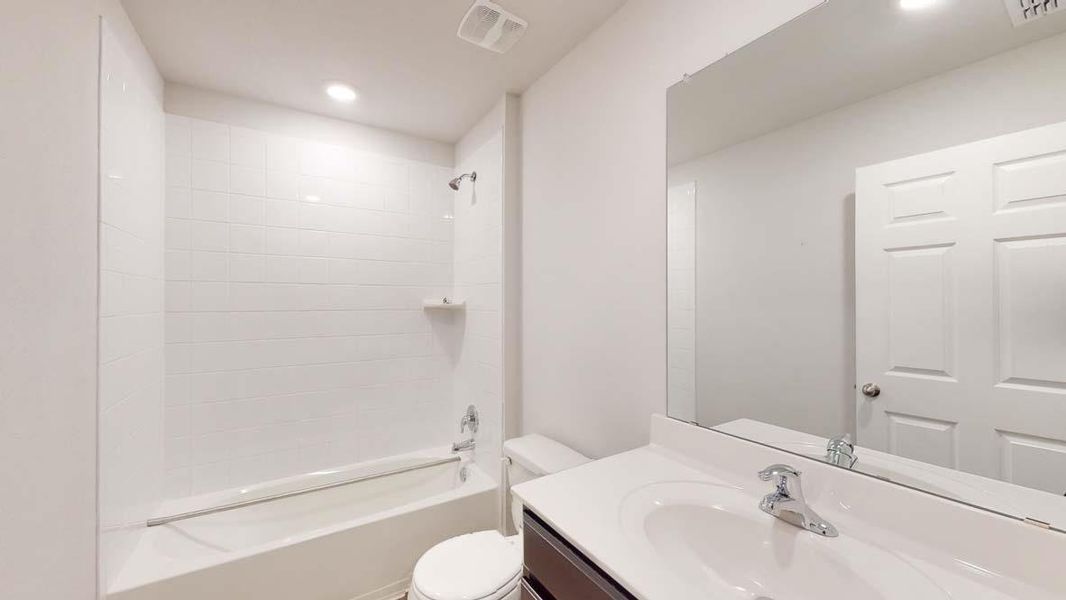 Full bathroom featuring a white subway tile tub surround, chrome fixtures, built-in shelf, and a vanity with a white countertop and integrated sink