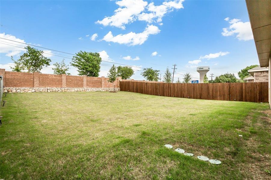 Spacious backyard with a well-maintained lawn, a privacy fence, and a brick wall