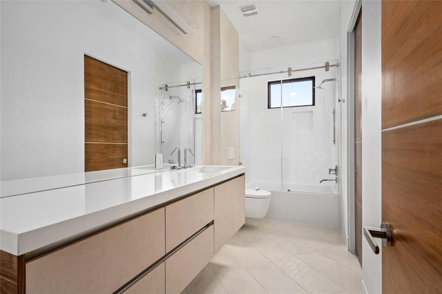 This secondary bathroom offers a sleek and modern design, featuring a large floating vanity with clean lines and ample counter space. The frameless glass shower door slides smoothly on a stylish stainless steel track, opening to a convenient shower/tub combo. The walls are accented with soft tile detailing, giving the room a polished and contemporary feel.