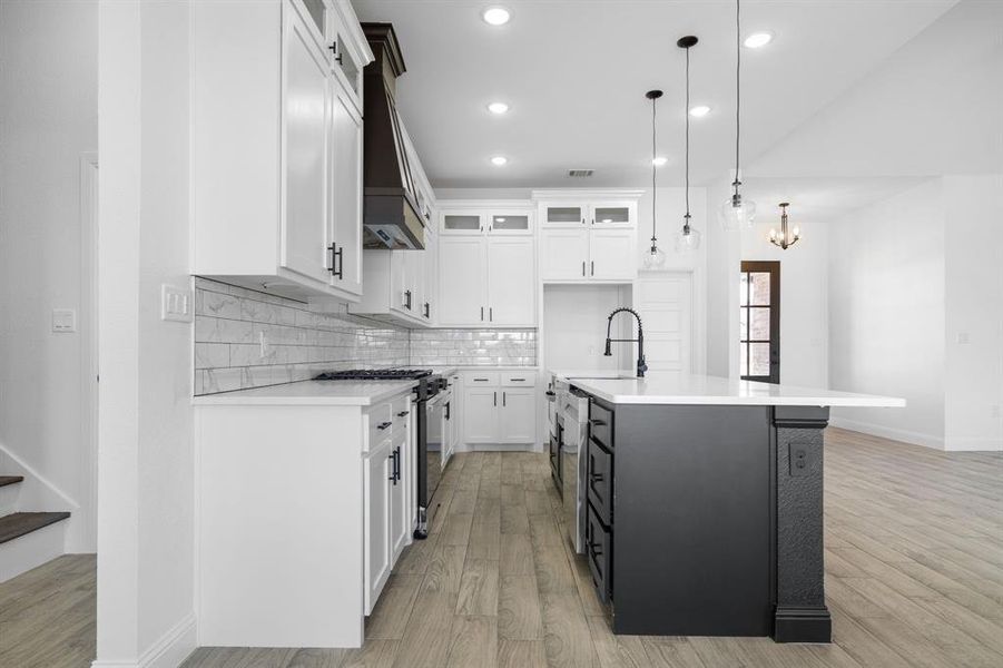 Kitchen with sink, white cabinets, hanging light fixtures, stainless steel range with gas stovetop, and a center island with sink