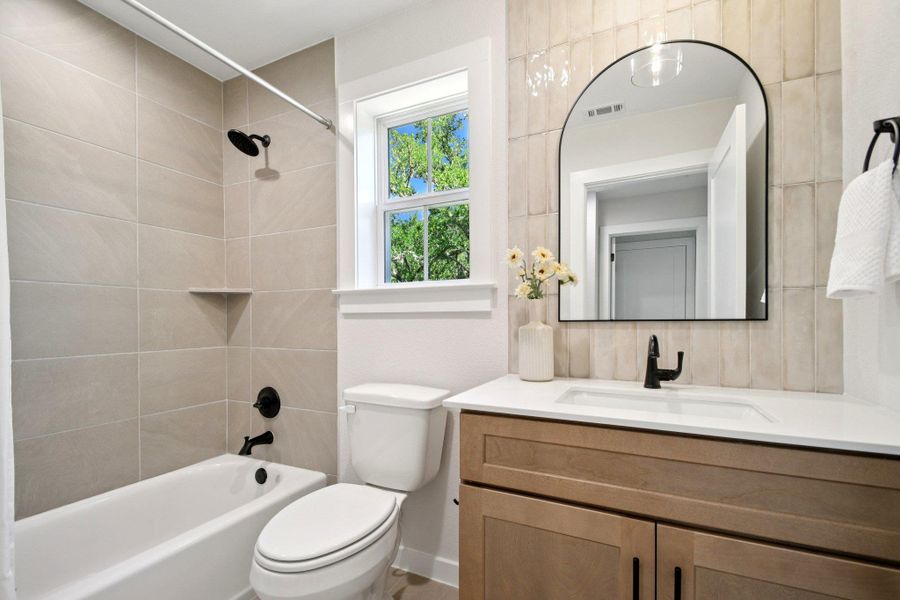 A well-lit bathroom features a vanity with a sleek sink and a contemporary tub with tiled surround. A well-lit bathroom features a vanity with a sleek sink and a contemporary tub with tiled surround.