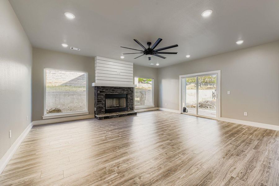 Unfurnished living room featuring light wood-style floors, a stone fireplace, recessed lighting, and a ceiling fan