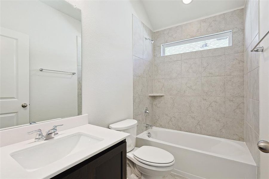 Full bathroom with tiled shower / bath combo, vanity, toilet, and vaulted ceiling