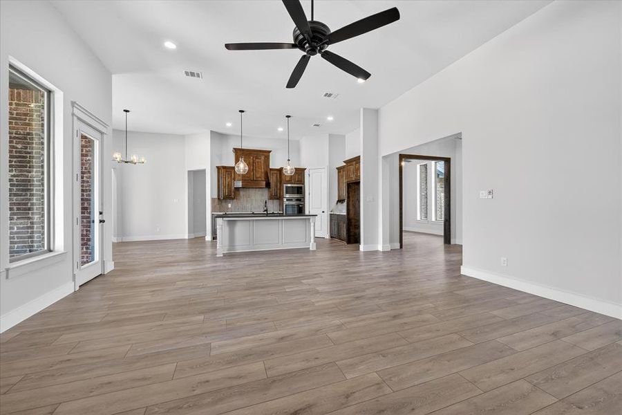 Unfurnished living room featuring hanging lights, ceiling fan, and light wood-style floors