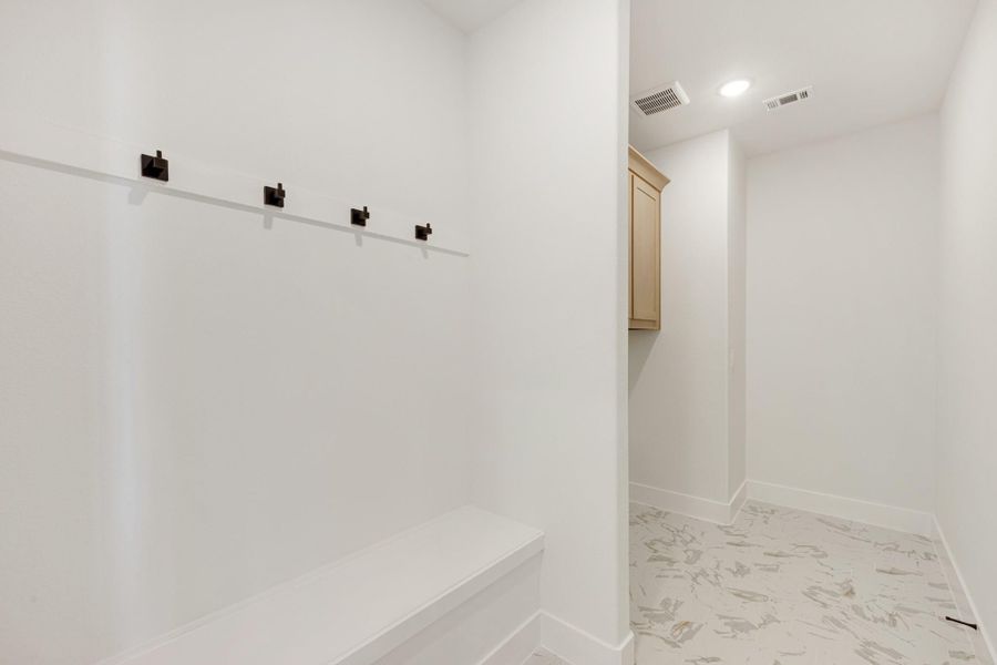 Mudroom with built-in bench, four dark metal coat hooks, and marble-look tile flooring