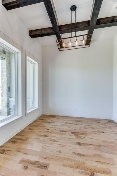 Spare room featuring light wood-type flooring, coffered ceiling, beamed ceiling, and a notable chandelier