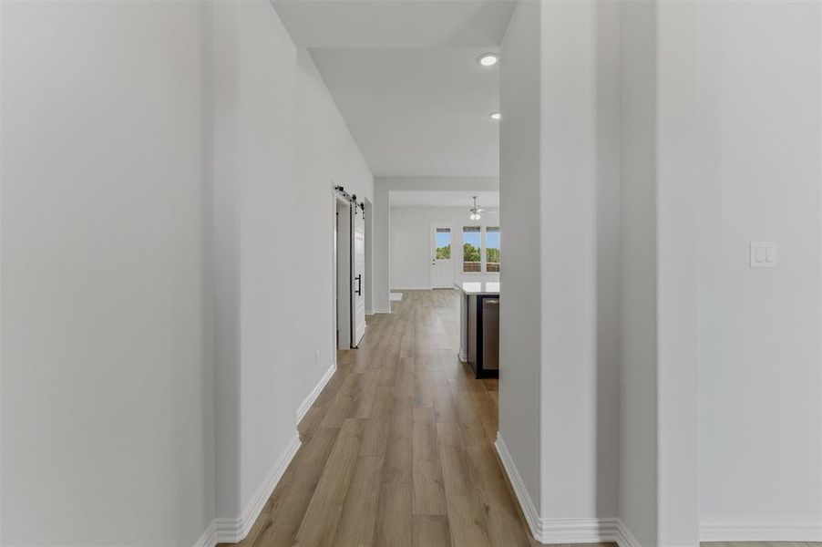 Hallway featuring wood-finish flooring, white baseboards, and barn doors with black hardware Hallway featuring wood-finish flooring, white baseboards, and barn doors with black hardware