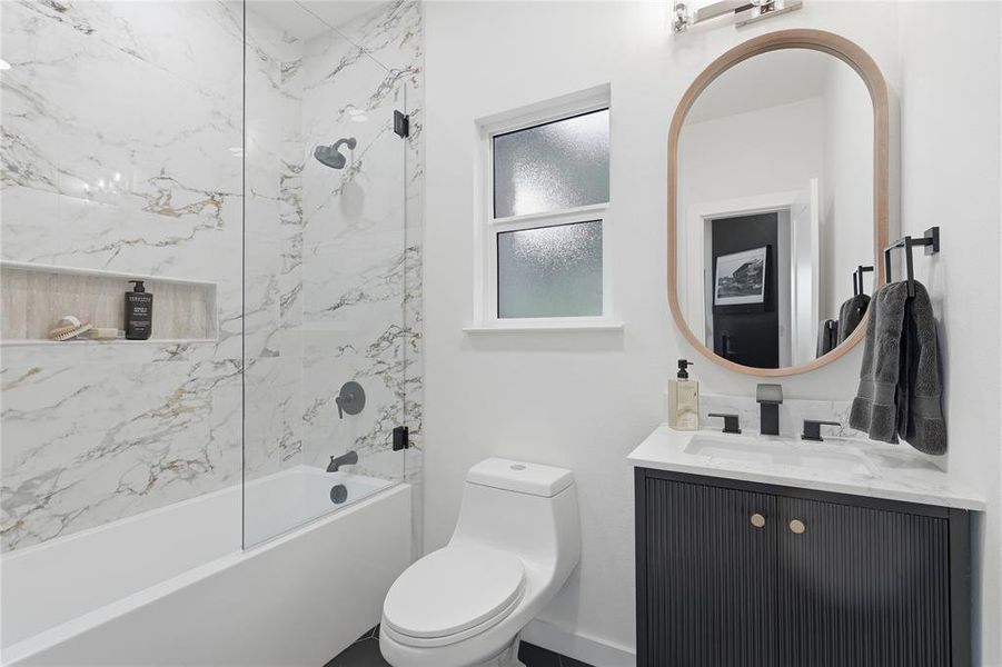 Bathroom featuring a full tub with glass enclosure, marble-style tile surround, and built-in shower niche