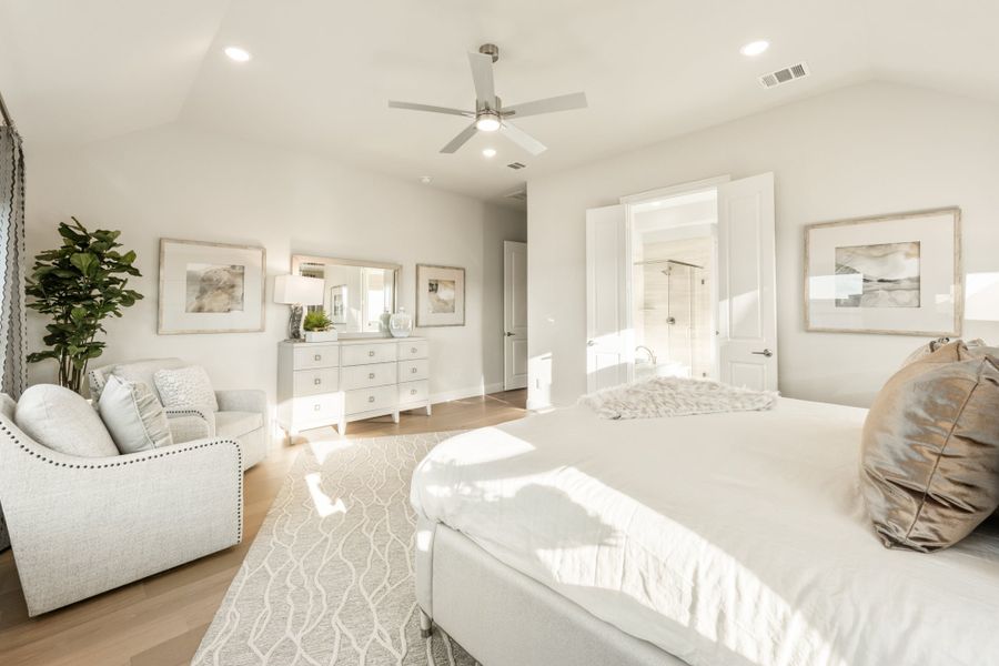 Bright master bedroom with ceiling fan, hardwood floors, white dresser, and open ensuite bathroom door