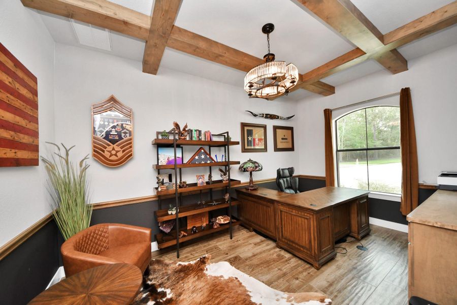 Charming home office featuring rustic wood beams, elegant lighting, and large window for natural light.