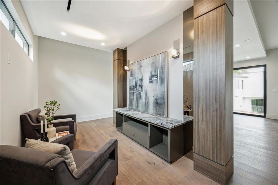 A sitting area in the primary bedroom is nestled beyond the wall, offering a tranquil space to unwind with a book or enjoy television. Enhanced by double sconce lights and custom-built-ins, this area provides both functionality and relaxation within the luxurious retreat.