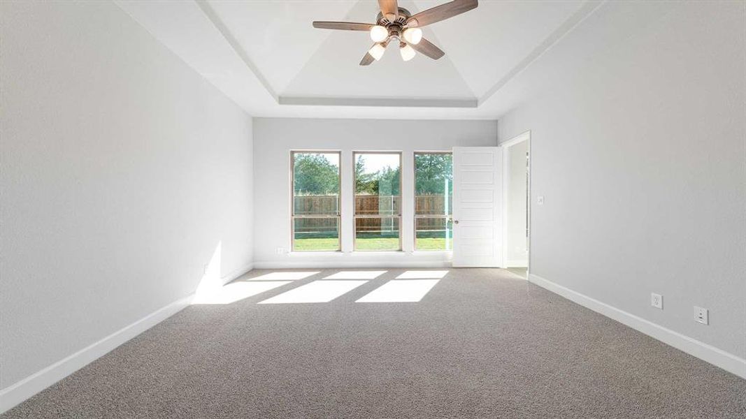 Carpeted empty room with ceiling fan and a tray ceiling