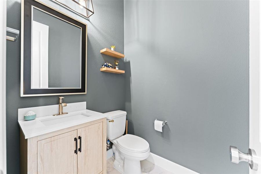 A well-appointed powder room featuring a light wood vanity with a white countertop and a gold-toned faucet