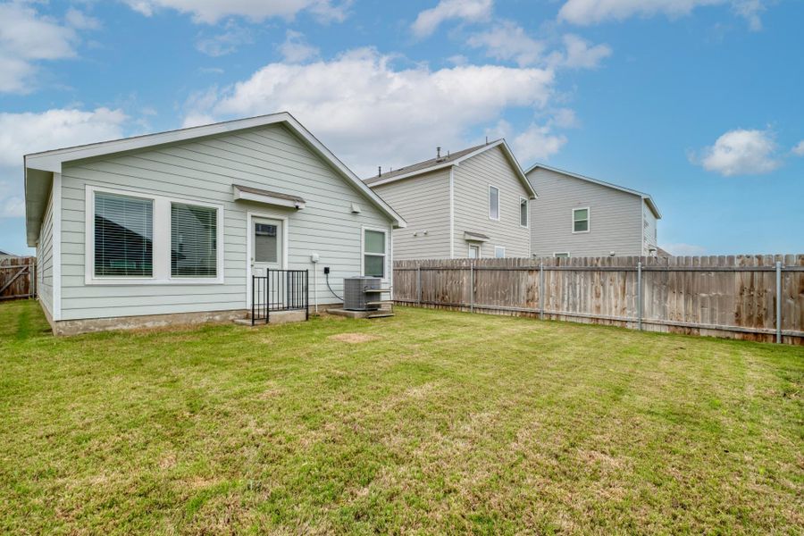 Expansive rear yard featuring green grass, a wood fence, and a light-colored siding exterior with multiple windows