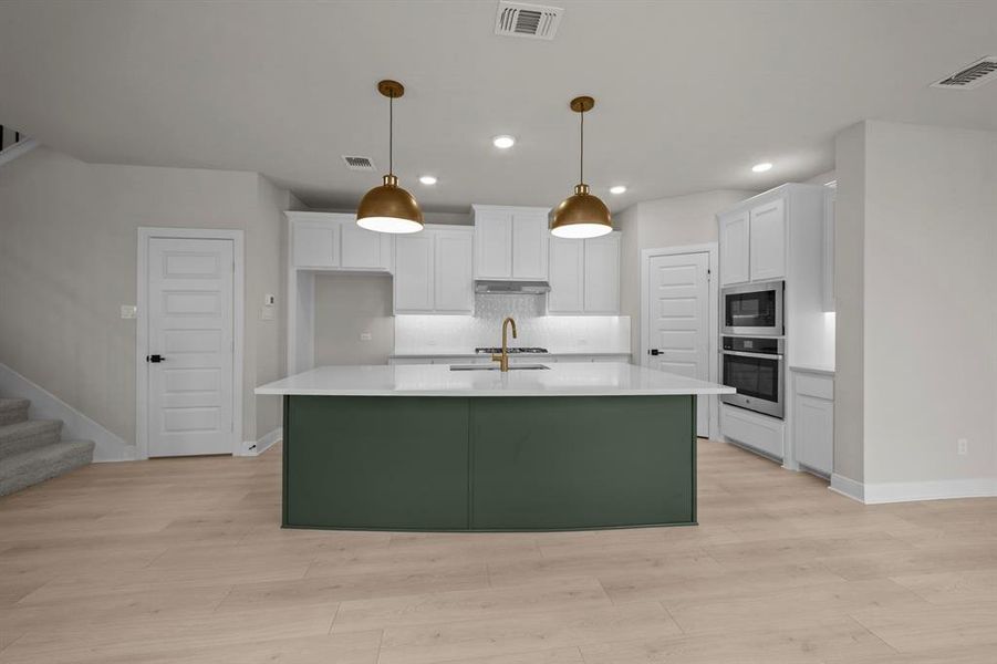 Kitchen featuring a center island with sink, stainless steel appliances, dual tone cabinets, pendant lighting, and light wood-style flooring
