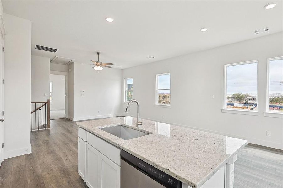 Kitchen with dishwasher, a kitchen island with sink, light hardwood / wood-style floors, light stone countertops, and sink