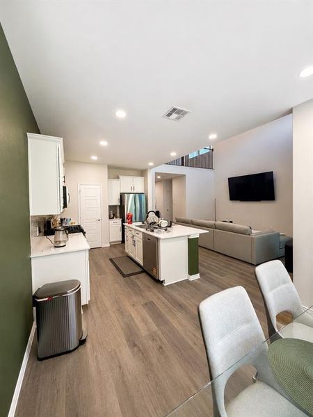 Open-concept kitchen and living area featuring wood-finish flooring, recessed lighting, white cabinetry, a kitchen island with seating, and stainless steel appliances