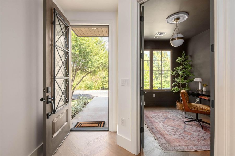 An inviting entrance foyer transitions seamlessly into a private study on herringbone patterned hardwood flooring. An inviting entrance foyer transitions seamlessly into a private study on herringbone patterned hardwood flooring.