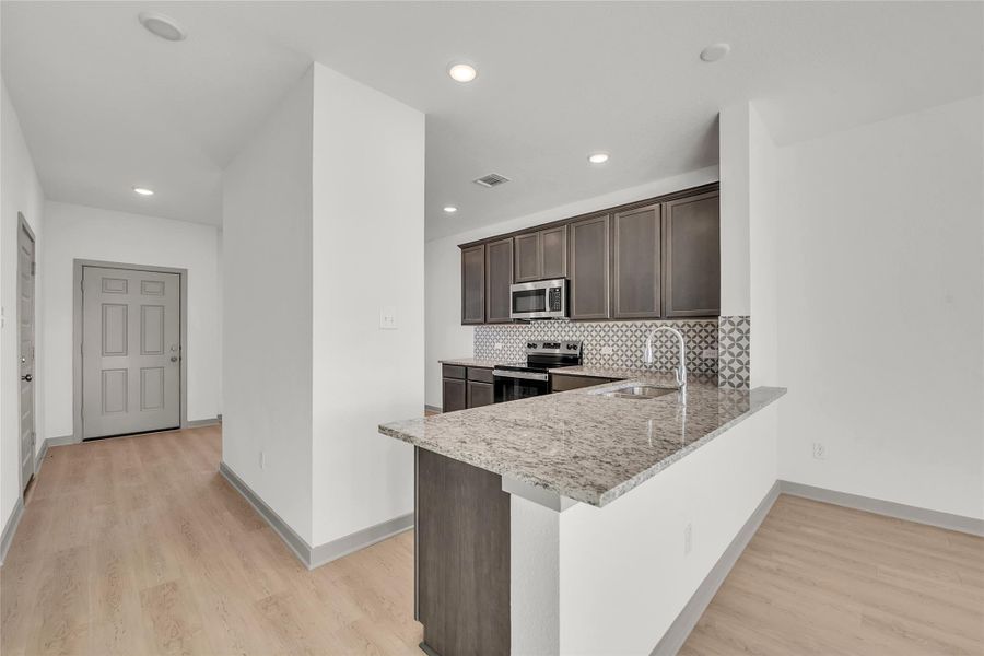 Kitchen with dark wood finish cabinets, stainless steel appliances, light stone counters, light wood-style flooring, and a peninsula