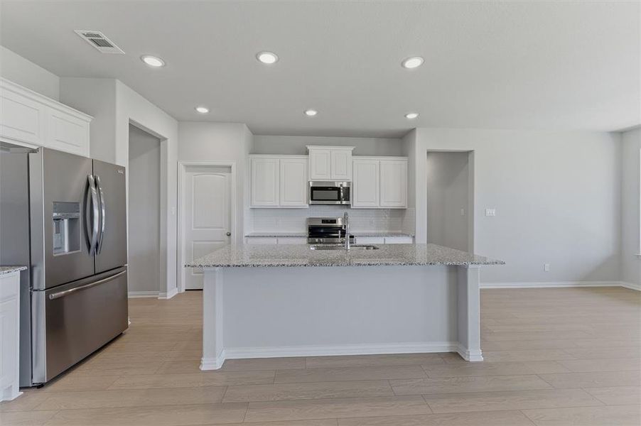 Kitchen with a central island featuring a light-toned countertop, stainless steel appliances, white cabinetry, recessed lighting, and wood-finish flooring Kitchen with a central island featuring a light-toned countertop, stainless steel appliances, white cabinetry, recessed lighting, and wood-finish flooring