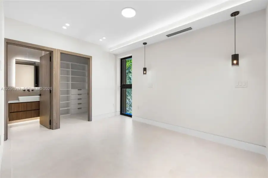 Interior space featuring large-format tile flooring, recessed ceiling lighting, dual pendant fixtures, and a walk-in closet with custom built-in shelving Interior space featuring large-format tile flooring, recessed ceiling lighting, dual pendant fixtures, and a walk-in closet with custom built-in shelving