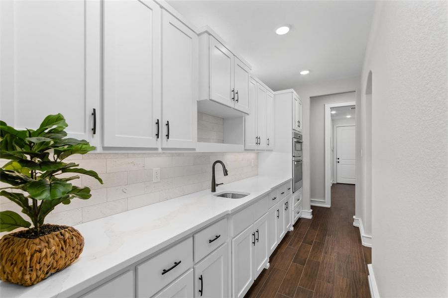 Kitchen with a sink, baseboards, white cabinets, recessed lighting, and light stone countertops Kitchen with a sink, baseboards, white cabinets, recessed lighting, and light stone countertops