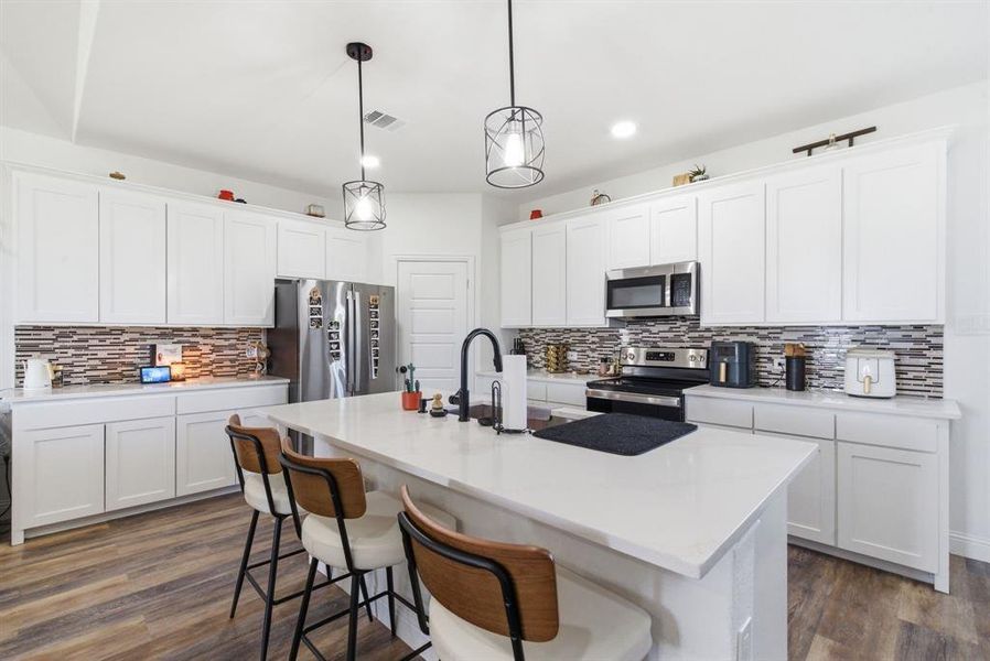 Kitchen with a breakfast bar area, white cabinets, dark wood-type flooring, and stainless steel appliances Kitchen with a breakfast bar area, white cabinets, dark wood-type flooring, and stainless steel appliances
