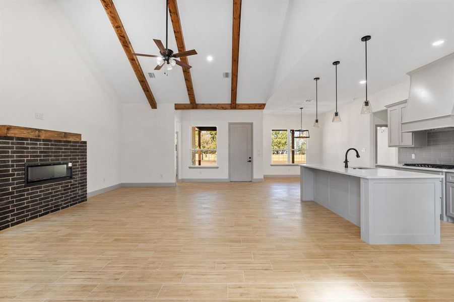Kitchen with open floor plan, a center island with sink, a tile fireplace, backsplash, and decorative light fixtures