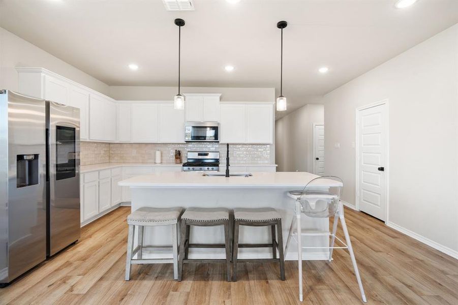 Kitchen featuring stainless steel appliances, pendant lighting, white cabinets, a kitchen bar, and recessed lighting Kitchen featuring stainless steel appliances, pendant lighting, white cabinets, a kitchen bar, and recessed lighting