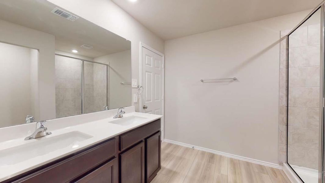 Bathroom featuring a dual vanity with dark wood-finish cabinetry and rectangular undermount sinks, a full-width mirror, a glass-enclosed shower with tiled walls, and wood-finish flooring