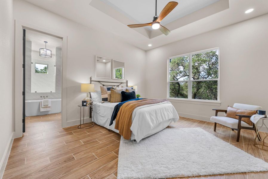 A well-appointed bedroom features a tray ceiling, recessed lighting, and a tree-filled view.