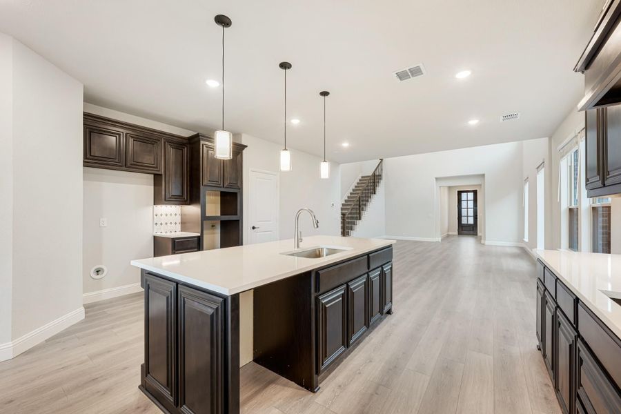 Kitchen with large center island, dark wood cabinets, pendant lights, and light hardwood floors open to living area