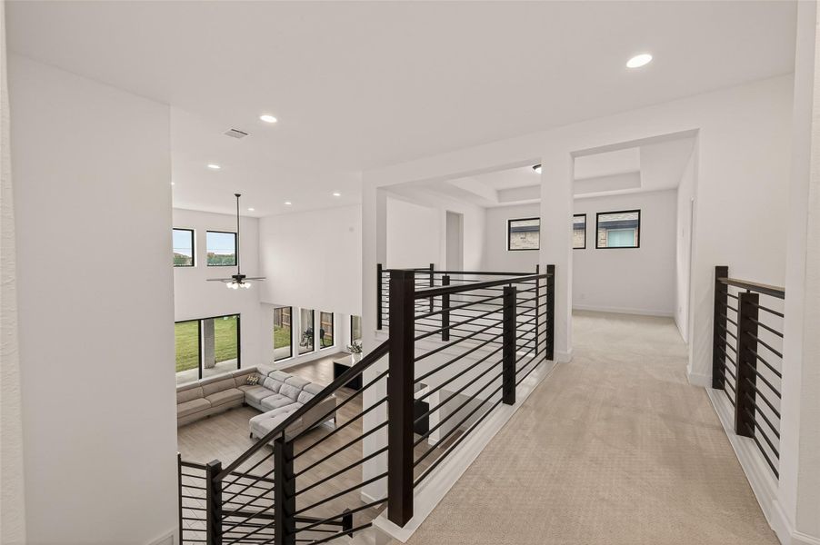 This photo showcases a modern, open-concept living area with high ceilings and large windows providing ample natural light. The space features a stylish railing on the upper level, overlooking a spacious living room with a sectional sofa. Neutral tones and contemporary design elements create a bright and inviting atmosphere.