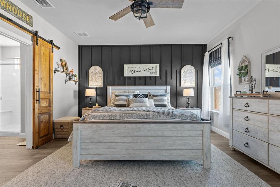 Bedroom with a barn door, ceiling fan, hardwood / wood-style floors, and ensuite bath