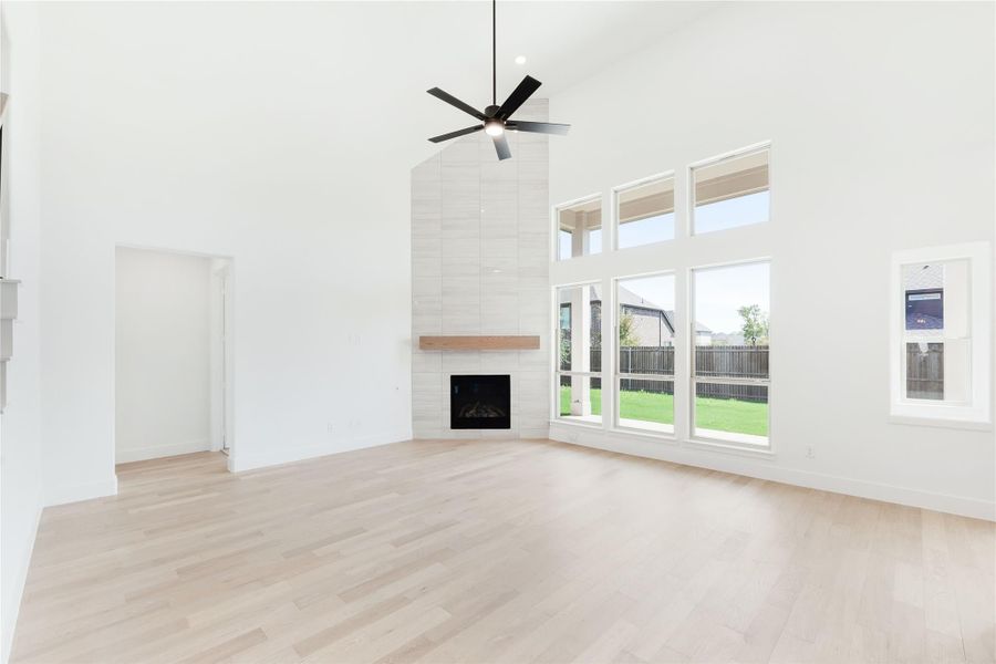 Open living room with vaulted ceiling, tile fireplace, ceiling fan, and large windows with backyard view