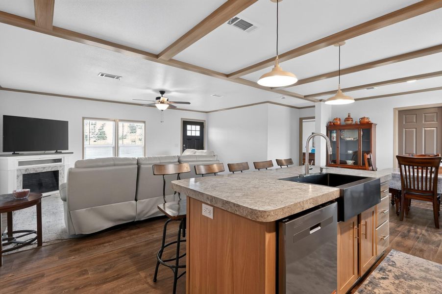 A contemporary kitchen and living area showcases an island with a farm sink, a fireplace, and rich wood-toned flooring.