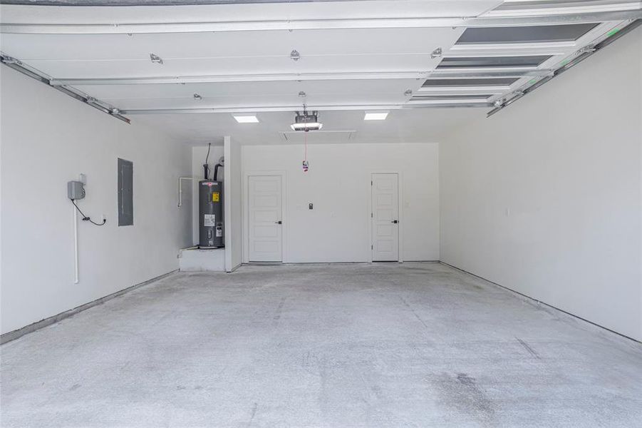 Garage featuring electric water heater, electric panel, and a garage door opener