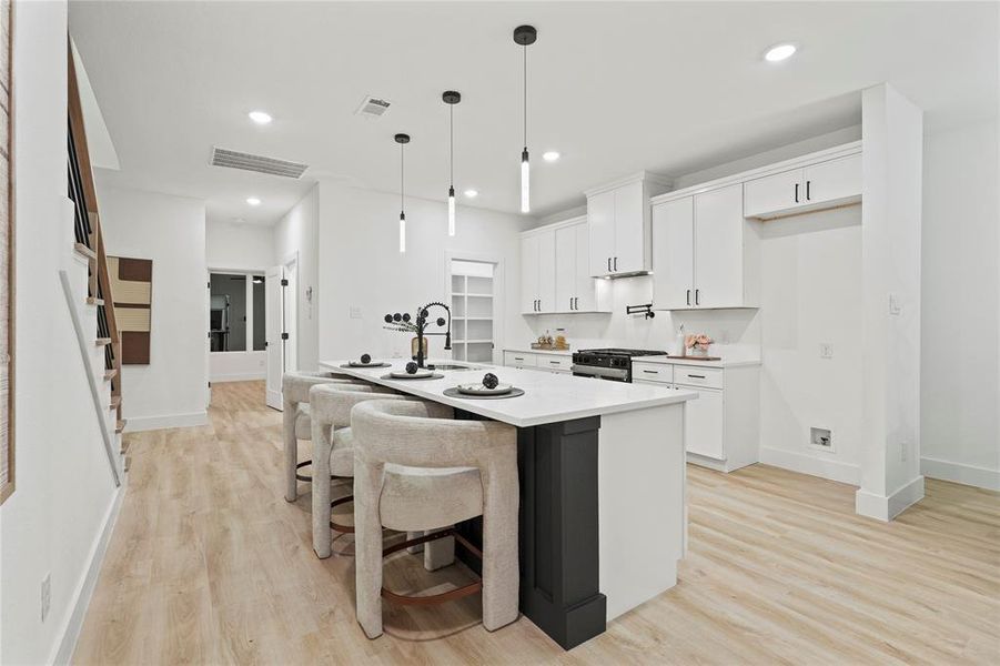 Kitchen with white cabinets, a breakfast bar area, light wood finished floors, a kitchen island with sink, and pendant lighting Kitchen with white cabinets, a breakfast bar area, light wood finished floors, a kitchen island with sink, and pendant lighting