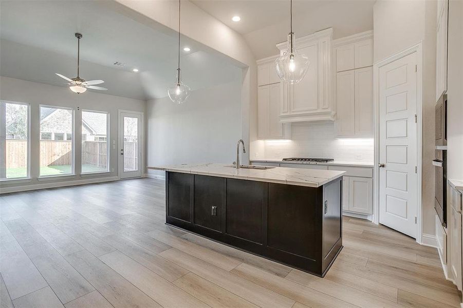 Kitchen featuring a kitchen island with sink, sink, vaulted ceiling, light wood-type flooring, and white cabinetry