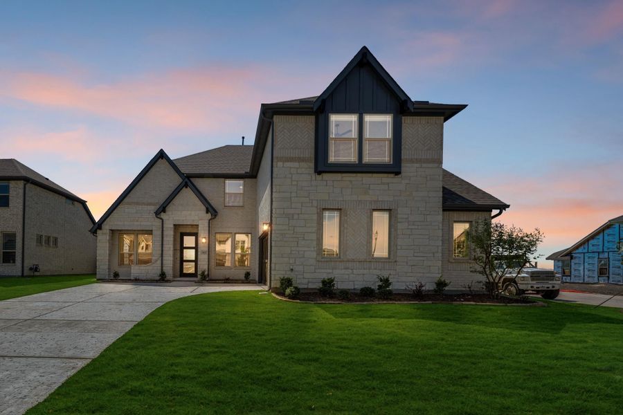 Two-story home with light stone exterior, dark trim accents, and manicured front lawn at dusk