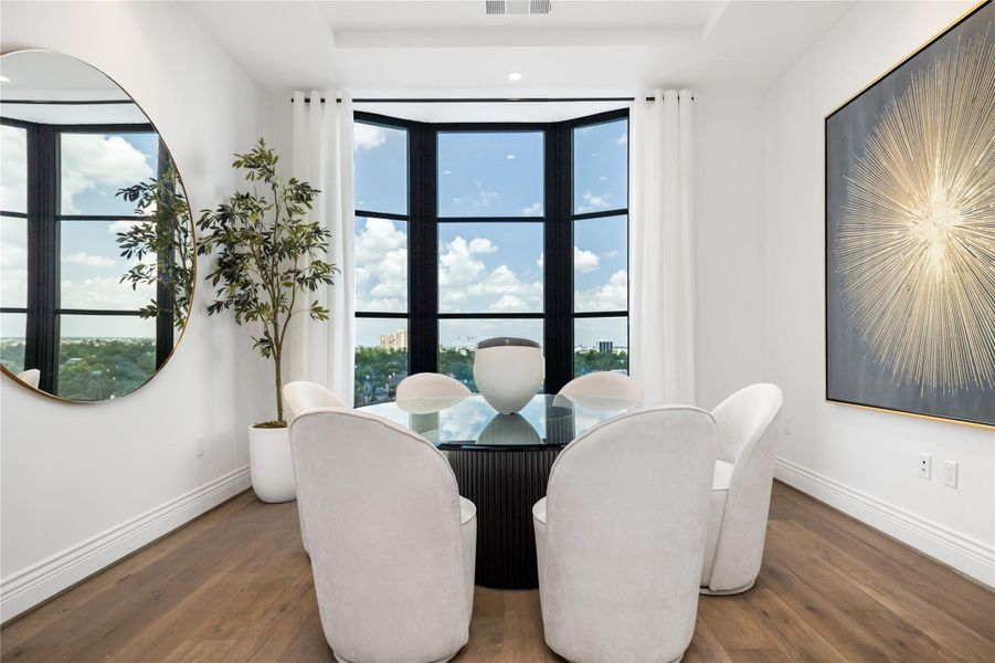 The dining area is framed by a dramatic bay of windows, offering elevated views and abundant natural light, creating a bright and inviting space for everyday dining or entertaining.