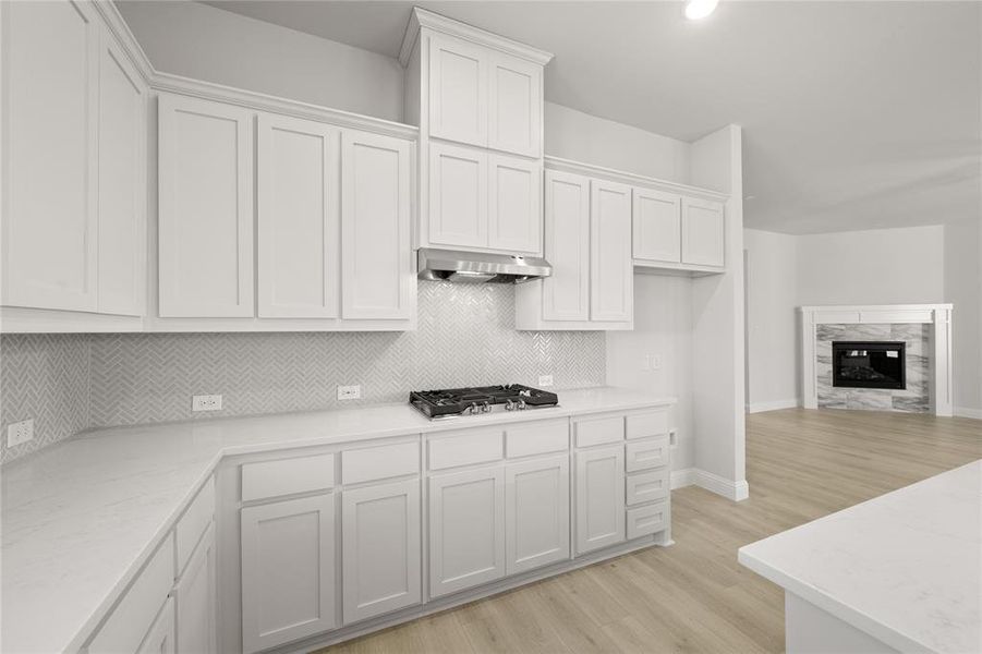 Kitchen with stainless steel gas stovetop, light wood-type flooring, a fireplace, range hood, and white cabinetry