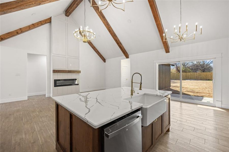Dual tone kitchen with a chandelier, a center island with sink, stainless steel dishwasher, light wood finished floors, and light stone counters