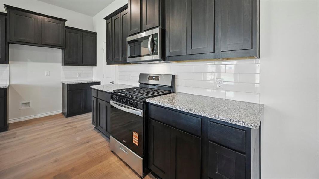 Kitchen featuring appliances with stainless steel finishes, light stone counters, backsplash, and light wood finished floors