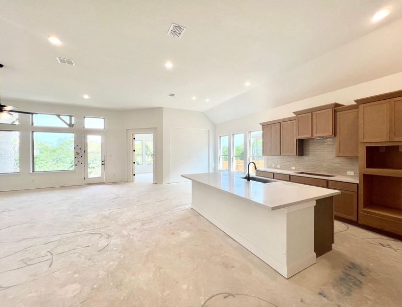 Kitchen with decorative backsplash, recessed lighting, an island with sink, lofted ceiling, and concrete flooring Kitchen with decorative backsplash, recessed lighting, an island with sink, lofted ceiling, and concrete flooring