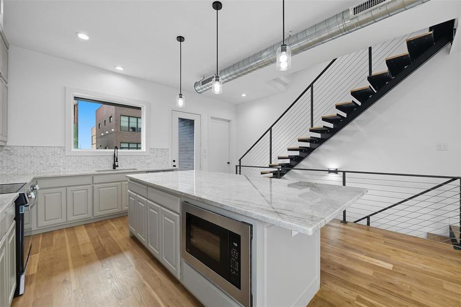 Kitchen featuring stainless steel microwave, light stone countertops, a center island, backsplash, and decorative light fixtures
