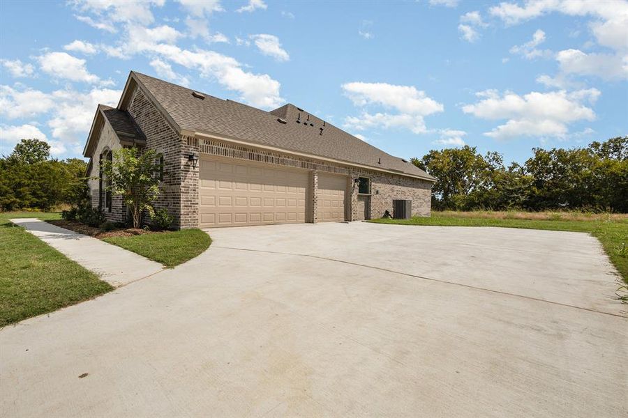 View of side of property with brick siding, roof with shingles, driveway, an attached garage, and a yard View of side of property with brick siding, roof with shingles, driveway, an attached garage, and a yard