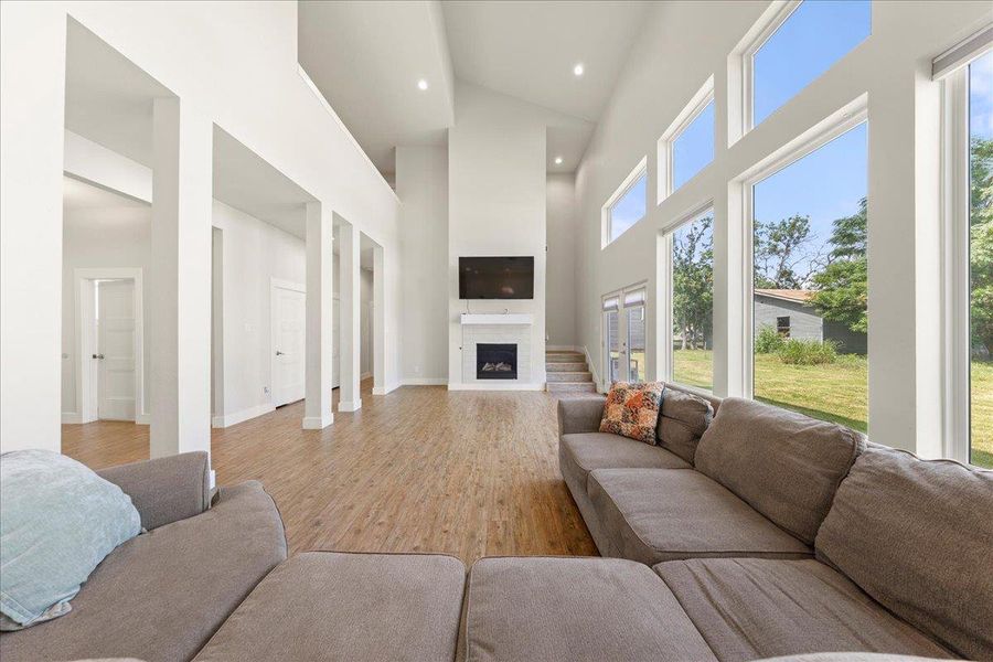 Living room featuring light wood finished floors, a towering ceiling, and a fireplace Living room featuring light wood finished floors, a towering ceiling, and a fireplace