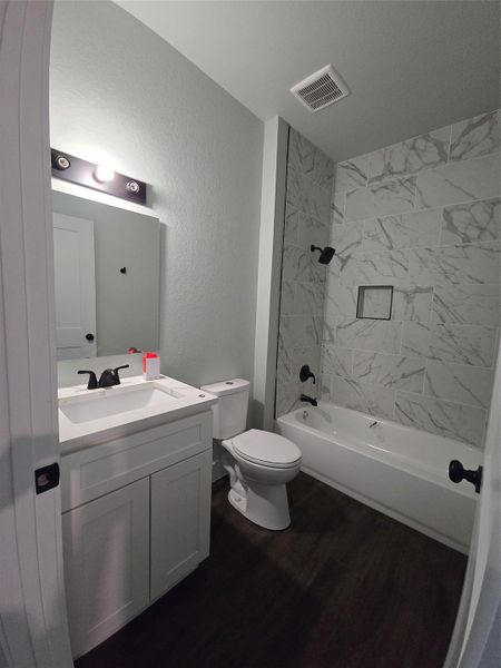 Full bath with bathing tub / shower combination, vanity, dark wood-type flooring, and a textured wall
